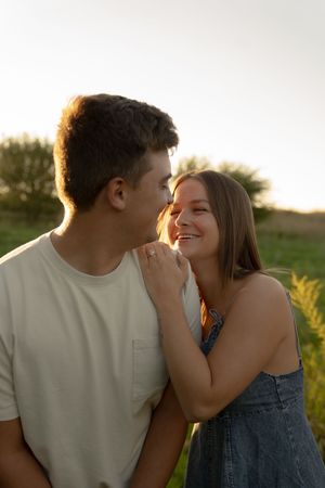 A romantic couple shares an intimate moment while laughing together in a sunlit field.
