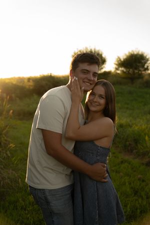 A couple embraces and smiles while posing in a field at sunset.