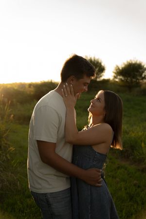 A tender moment between a couple in casual attire standing in a grassy field at sunset.