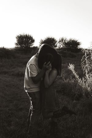 A black and white photo of a couple embracing in a rural setting at dusk.