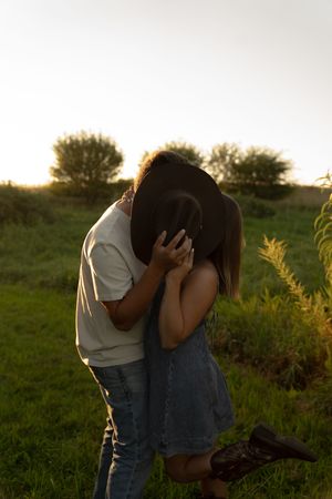 Romantic couple embracing in a grassy field at sunset with golden light filtering through the trees.