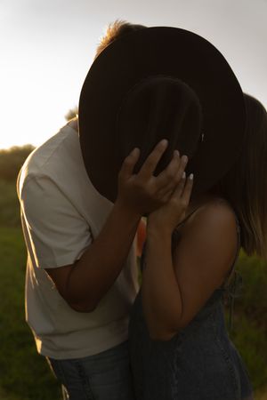 Silhouetted figures in an embrace during sunset in a meadow setting.