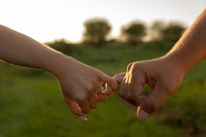 Close-up of hands reaching toward each other against a blurred natural background.