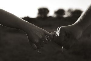 Dramatic silhouette of hands connecting against a dark background outdoors.