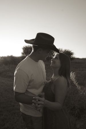 A romantic black and white portrait of a couple embracing at sunset in a field.
