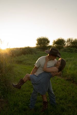 A couple shares an intimate dip pose against a golden sunset in a grassy field.