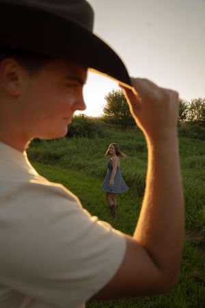 Silhouette of someone in a cowboy hat framing a figure twirling in a sundress at sunset.