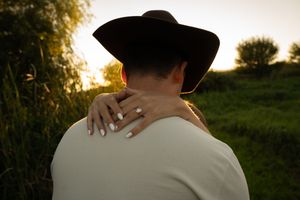 Back view of a couple embracing in a field at sunset with a cowboy hat visible.
