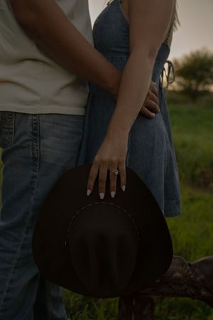Detail shot of a couple holding a black cowboy hat while wearing jeans and boots.
