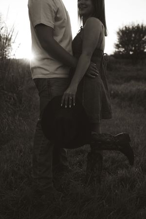 Black and white silhouette of a couple standing close together in a field at sunset.