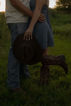 Intimate moment captured between a couple with cowboy boots and hat at dusk.
