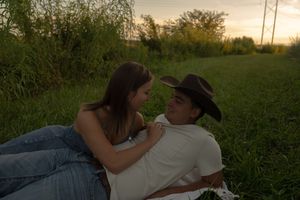 Couple sharing an intimate moment while lying on a blanket in a grassy field at sunset.