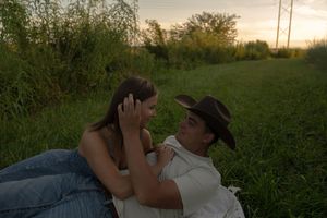 A couple lies together in a grassy field at sunset with warm golden light.