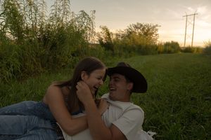 Two people share an intimate moment in a meadow during golden hour.