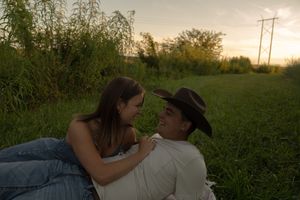 Silhouettes of a couple relaxing in tall grass with utility poles in the background.