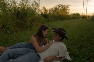 A romantic scene unfolds in a rural field as the sun sets behind trees.