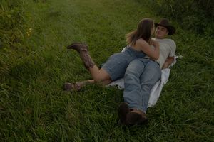 Two people share a tender moment while lying in green grass outdoors.