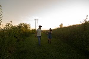 Two figures walk along a hilltop silhouetted against a sunset sky.