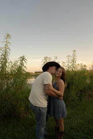 A romantic couple shares a tender moment at sunset in a field of tall grass.
