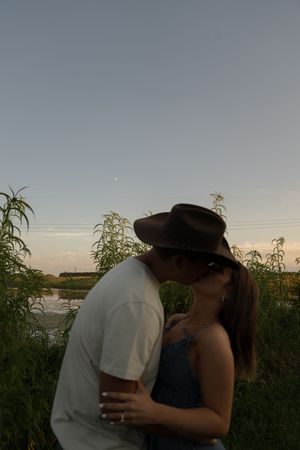 Two people embrace lovingly against a sunset backdrop in nature.