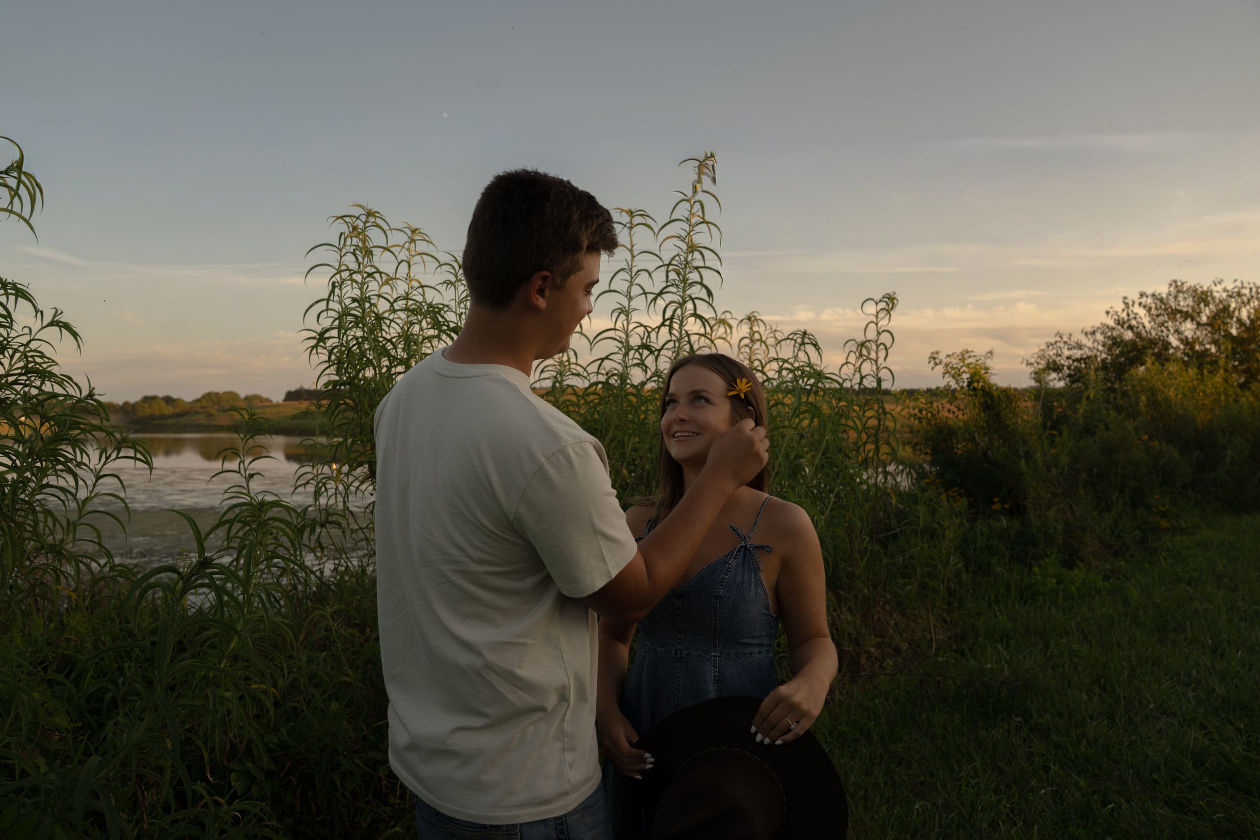 Wedding couple embraces during sunset photoshoot with scenic rural backdrop.