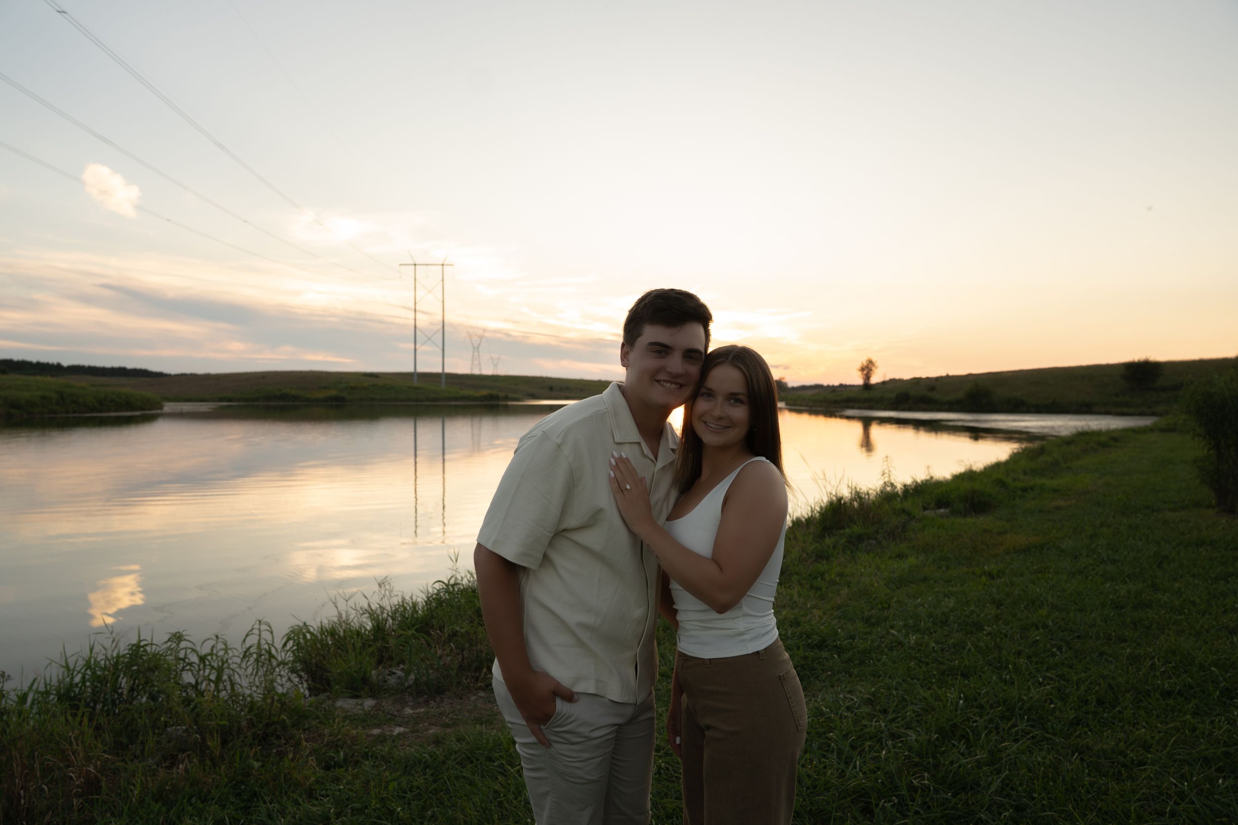 A couple stands together on grassy shores during golden hour.