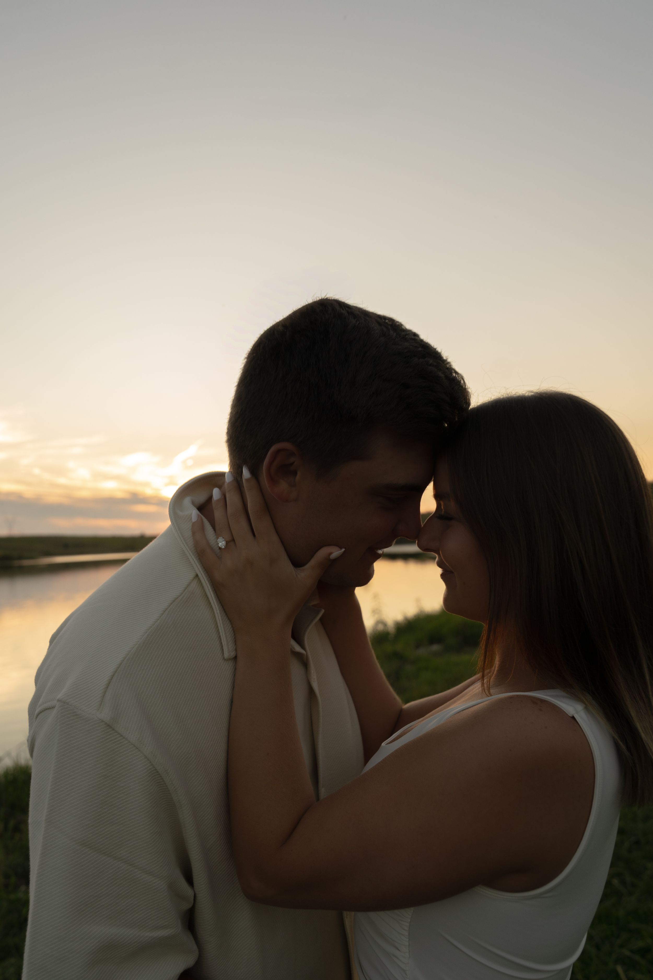 Two people share an intimate moment at sunset by the water's edge.