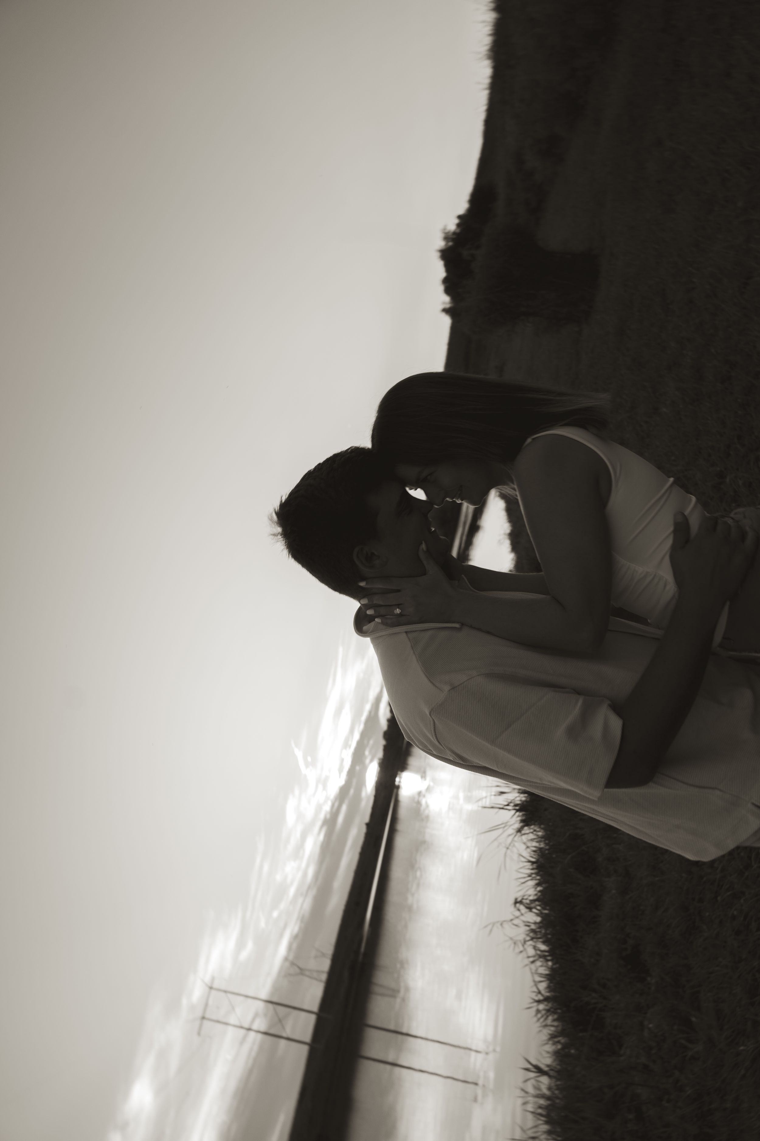 Two figures stand close together by a lake during sunset.