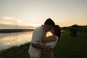 A couple shares an intimate moment on a lakeside hill during golden hour.