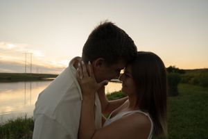 Two people embrace on a grassy slope with a sunset lake view.
