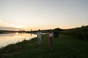A distant view of a couple on a hillside during sunset by a lake.