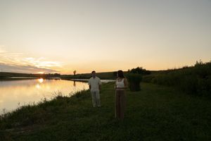 A romantic couple shares a tender moment on a grassy hillside at sunset.
