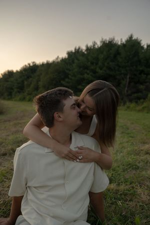 Two people in light-colored clothing embrace on a grassy slope at dusk.