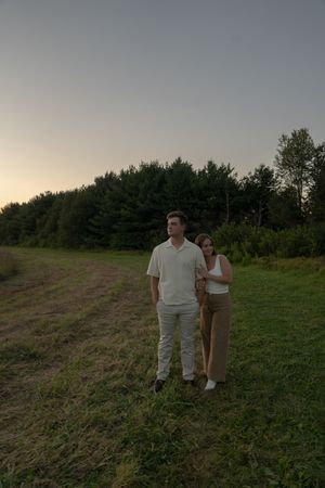 Two people stand together on a grassy hillside during sunset.
