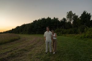 A couple stands silhouetted against a sunset sky on a hilltop.
