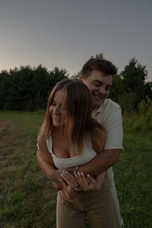 A romantic couple embraces in a grassy field at sunset, sharing intimate moments together.