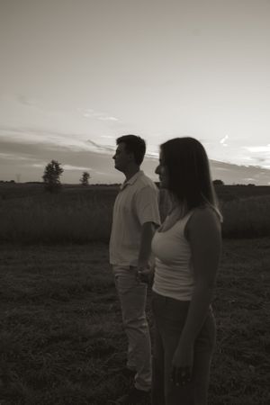 Two silhouettes stand against a dramatic black and white sunset sky in an open field.