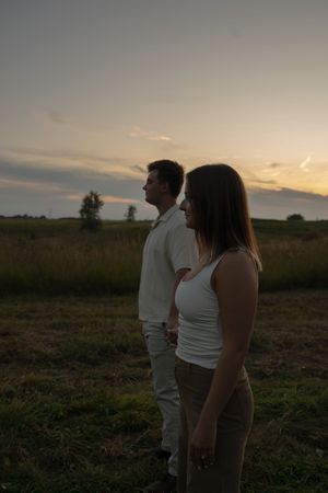 A couple watches the sunset together in a rural field during dusk.