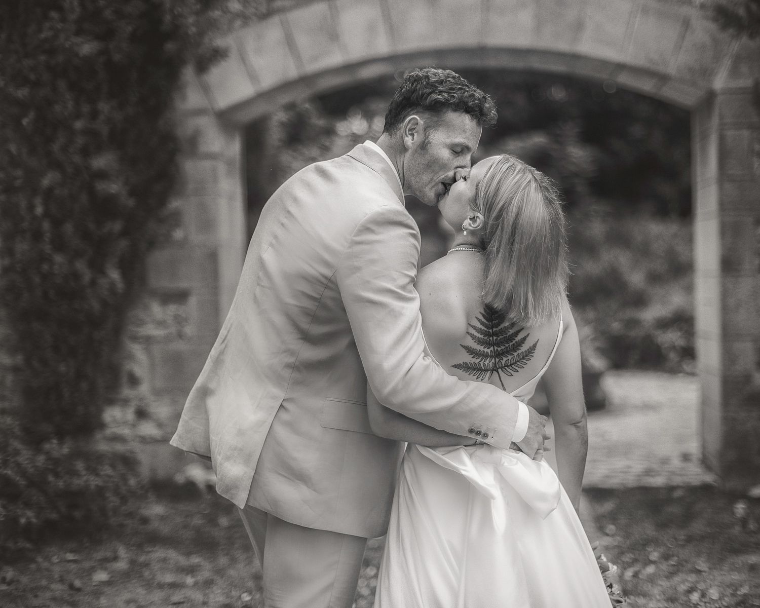 Photographe mariage Montauban – cliché en noir et blanc d’un couple de mariés s’embrassant sous une arche de pierre, Laetitia KLOPOCKI