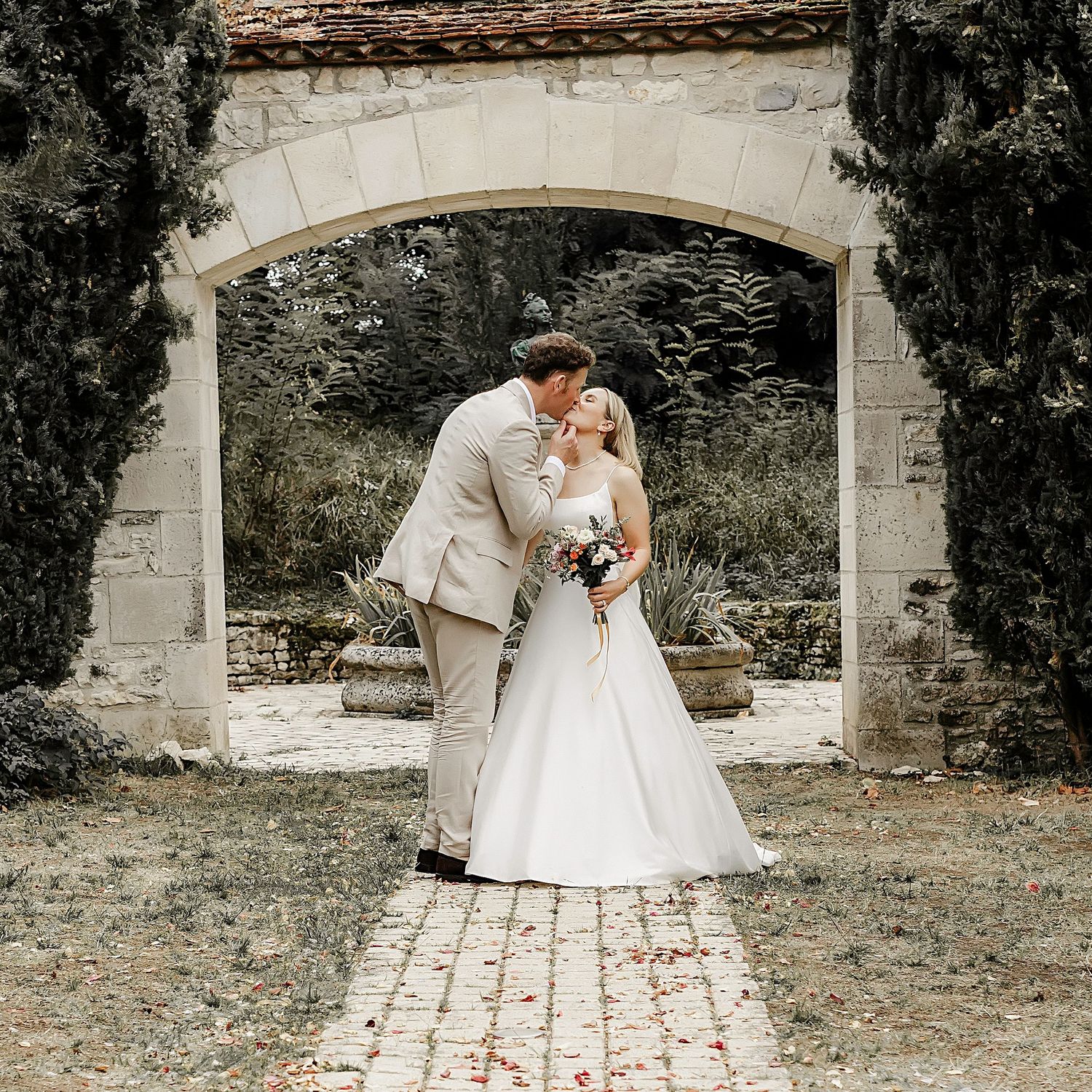 Mariage élégant au château près de Montauban – un couple s’embrasse sous une arche en pierre, photographié par Laetitia Klopocki,