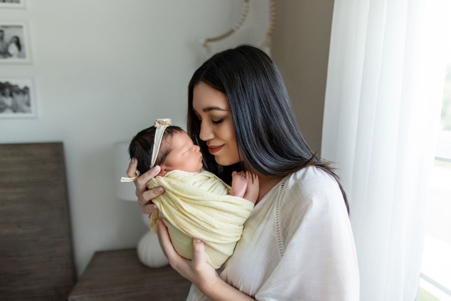 A figure in a gray cardigan cradles and tenderly kisses a newborn baby wrapped in a pale yellow blanket.