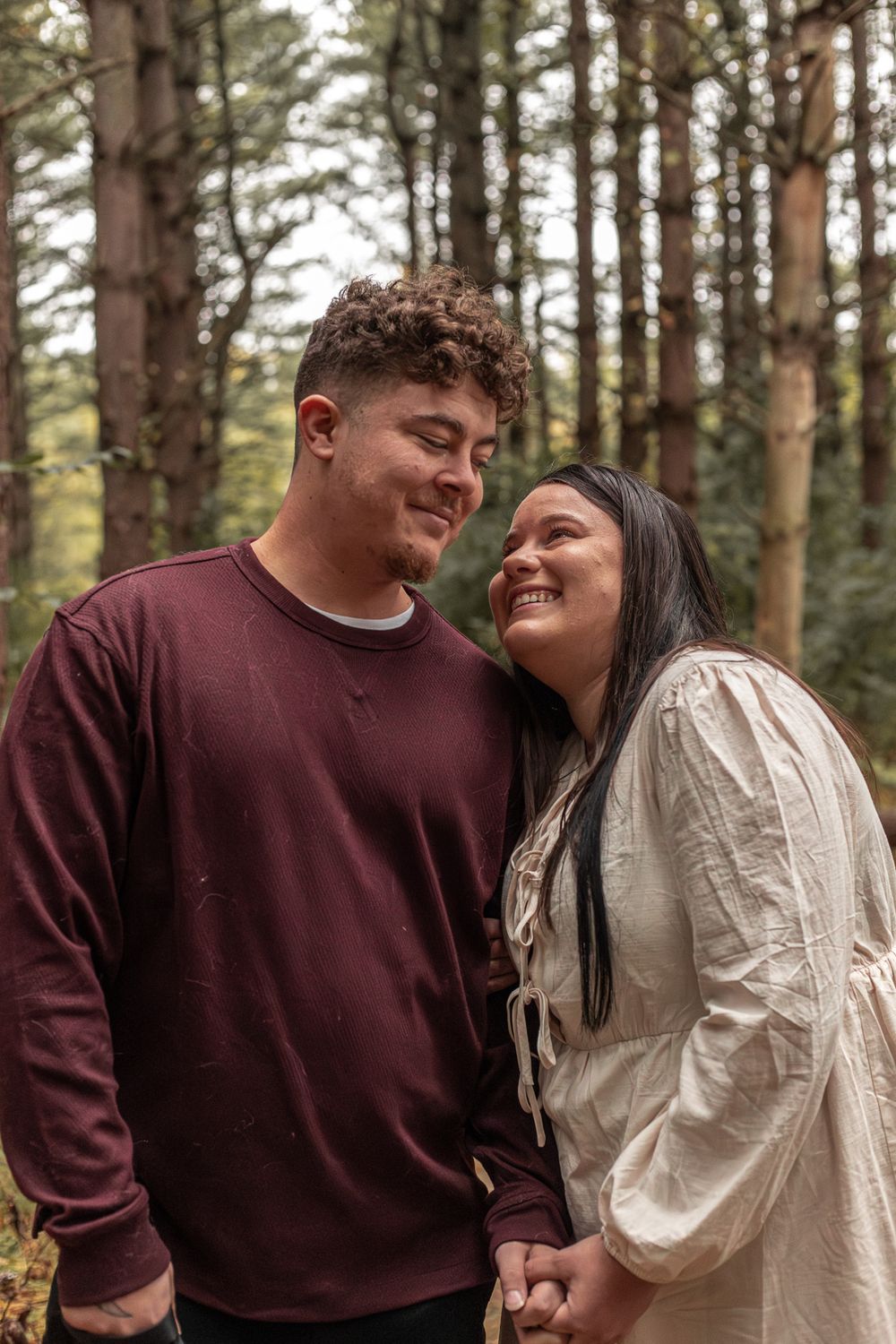Couple sharing joyful moment among tall pine trees in autumn forest.
