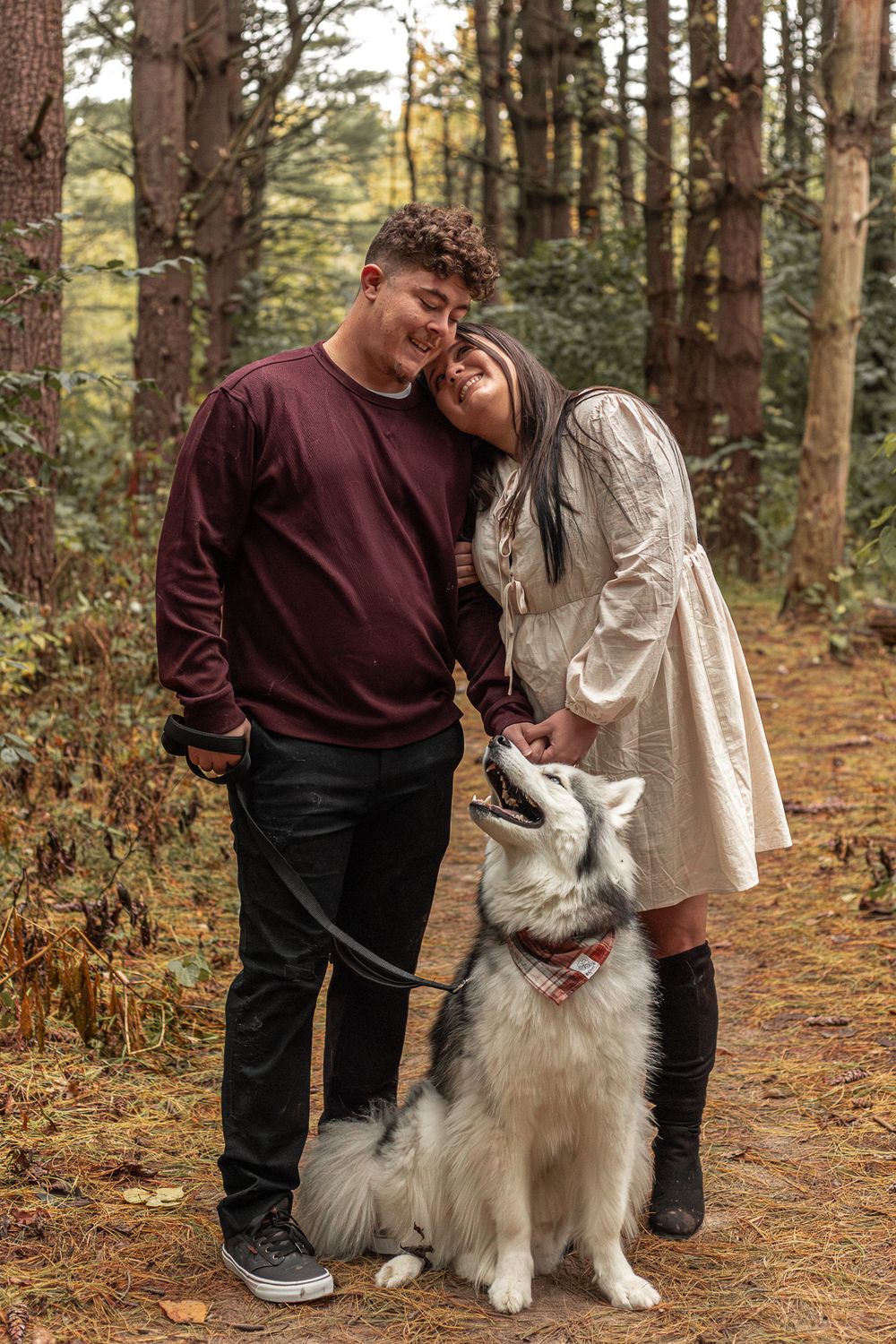 Happy couple with their fluffy white dog on forest trail among pine trees.