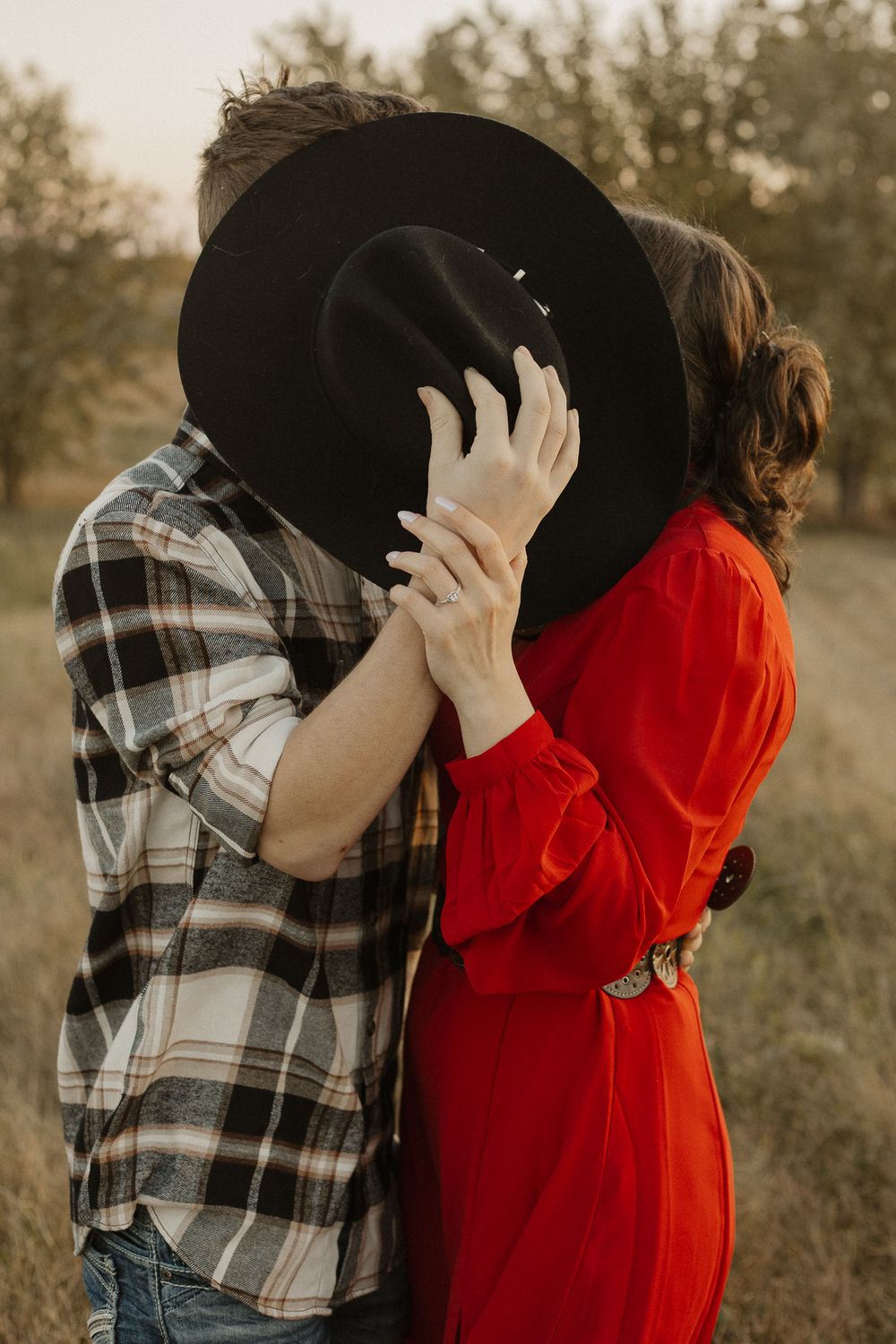 Romantic couple in plaid shirt and red sweater sharing an intimate moment in a golden field at sunset.