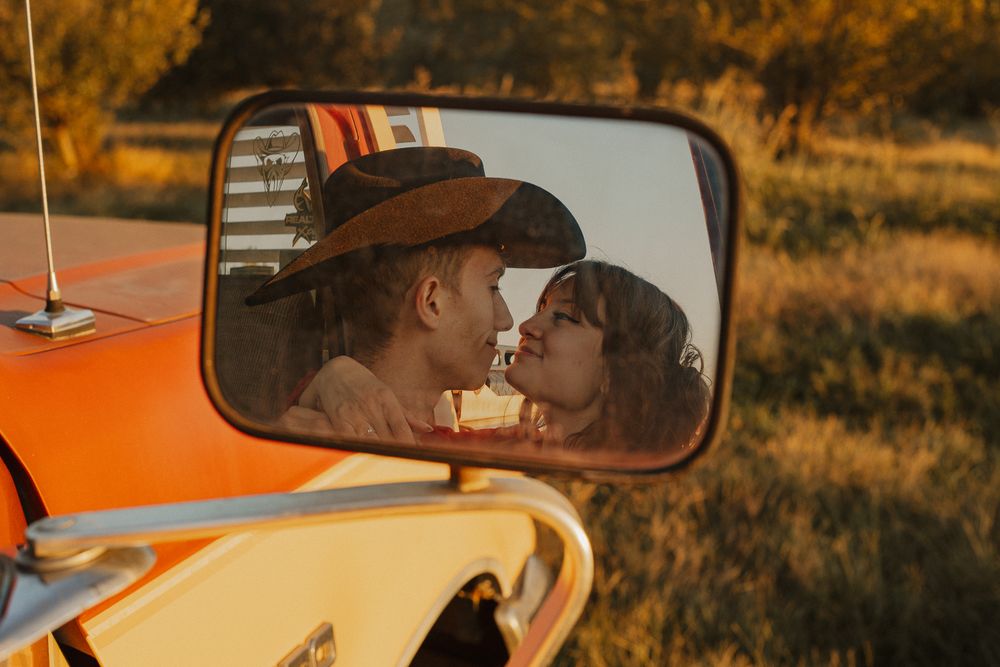 Couple sharing a tender moment in an orange vintage car during golden hour.