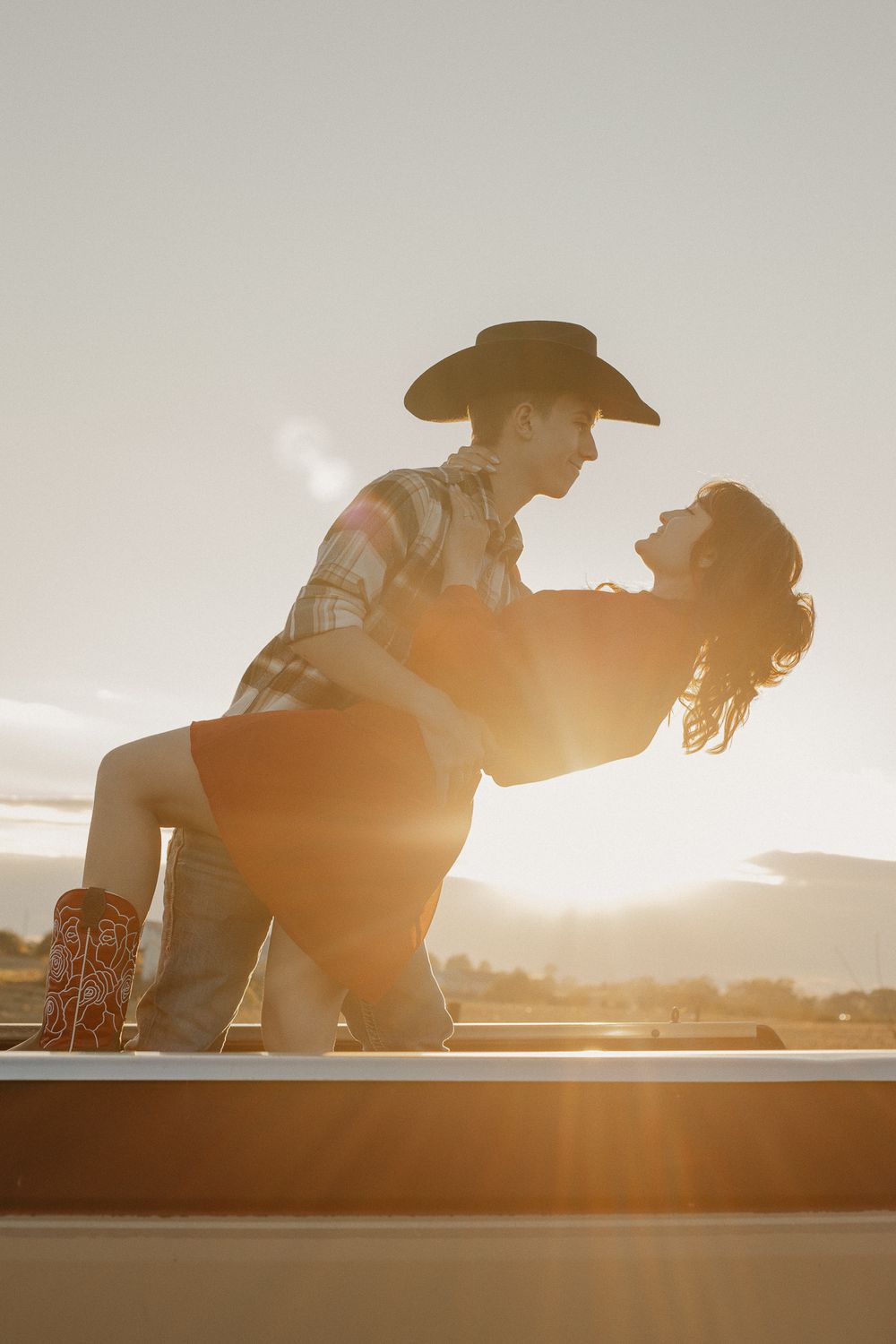 Silhouettes of a couple in cowboy hats against a bright sunset backdrop.