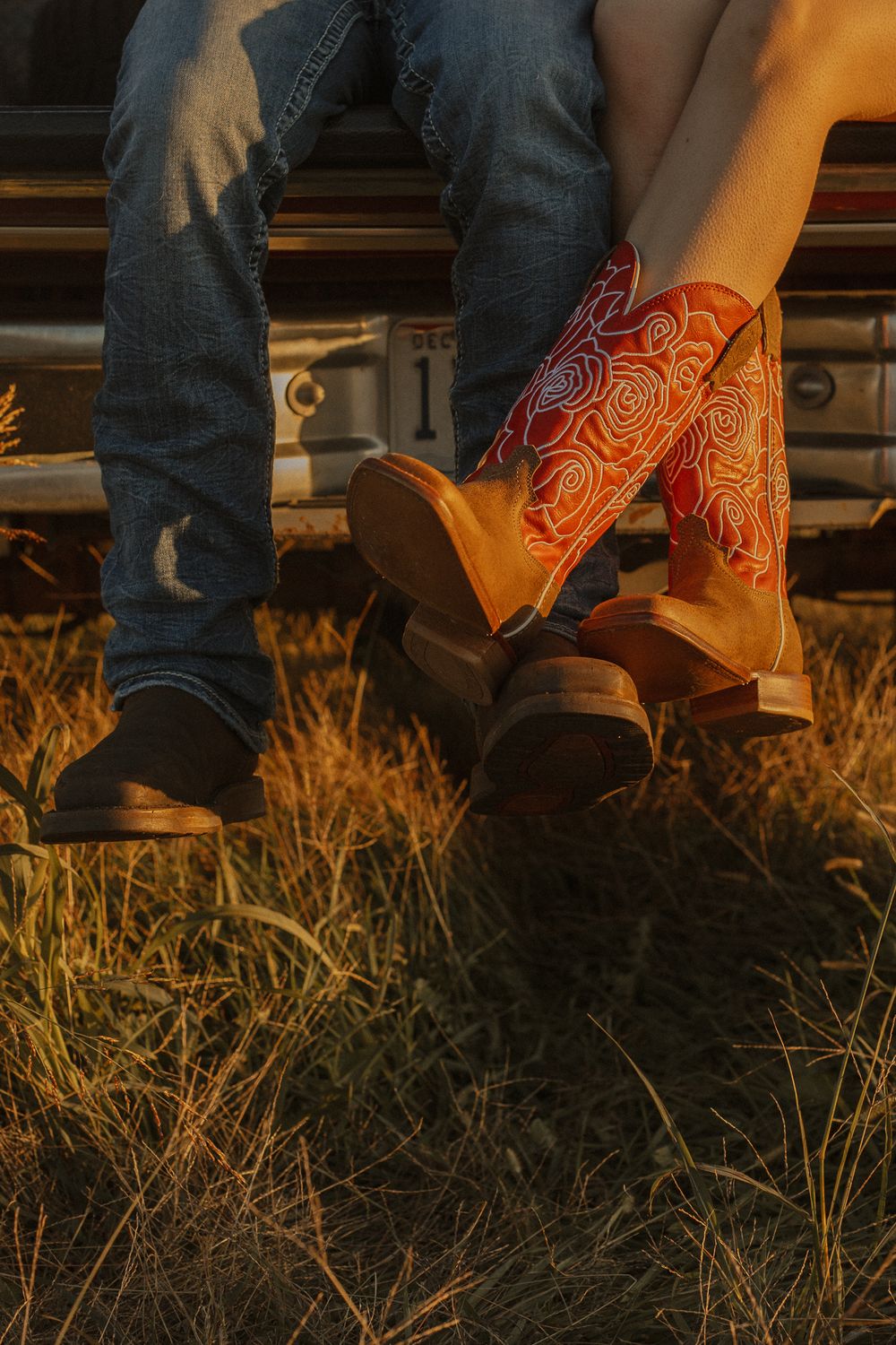 Close-up of cowboy boots and jeans sitting on rustic wooden steps at sunset.
