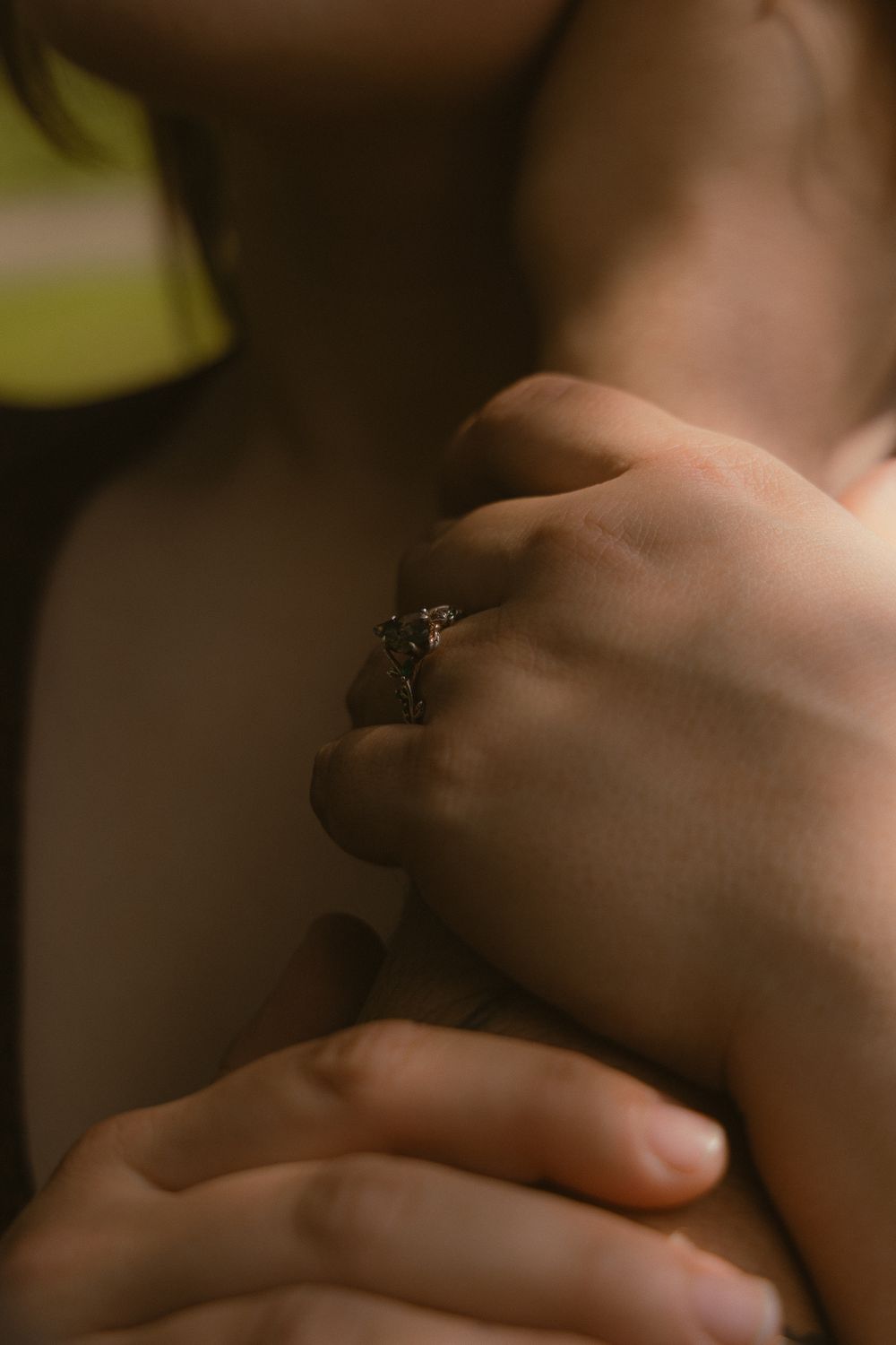Close-up of hands embracing with a decorative silver ring, captured in warm, moody lighting.