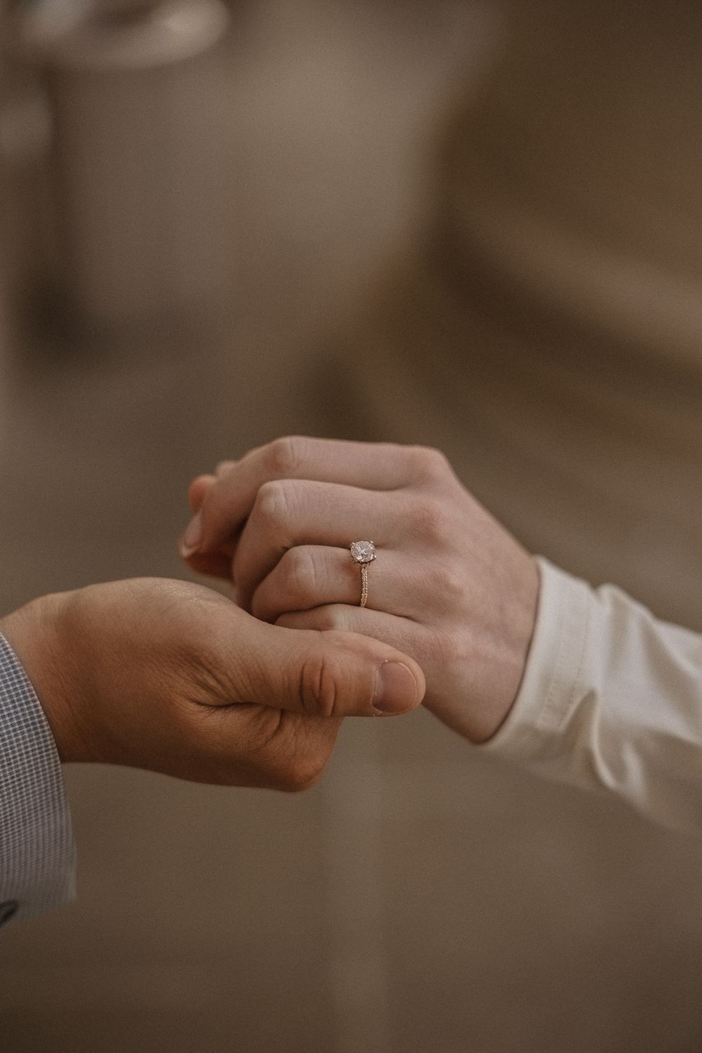 Close-up of hands reaching for each other with engagement ring visible in warm lighting.