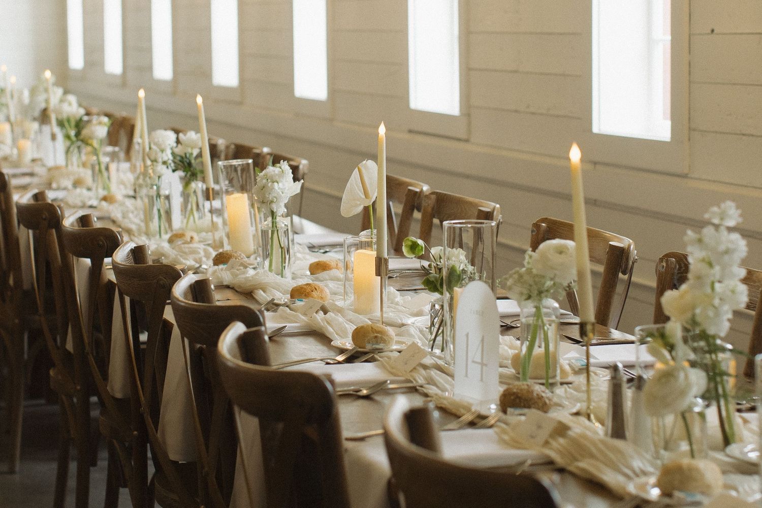Elegant wedding reception tables set with white linens and floral centerpieces in natural light.